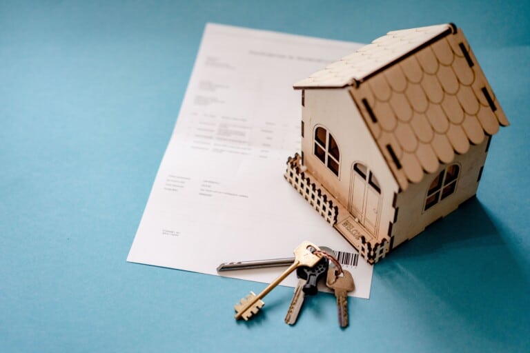 A set of house keys resting beside a small model house and a welcome sign