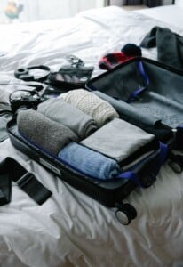 An open suitcase on a bed being packed with neatly folded clothes and travel essentials