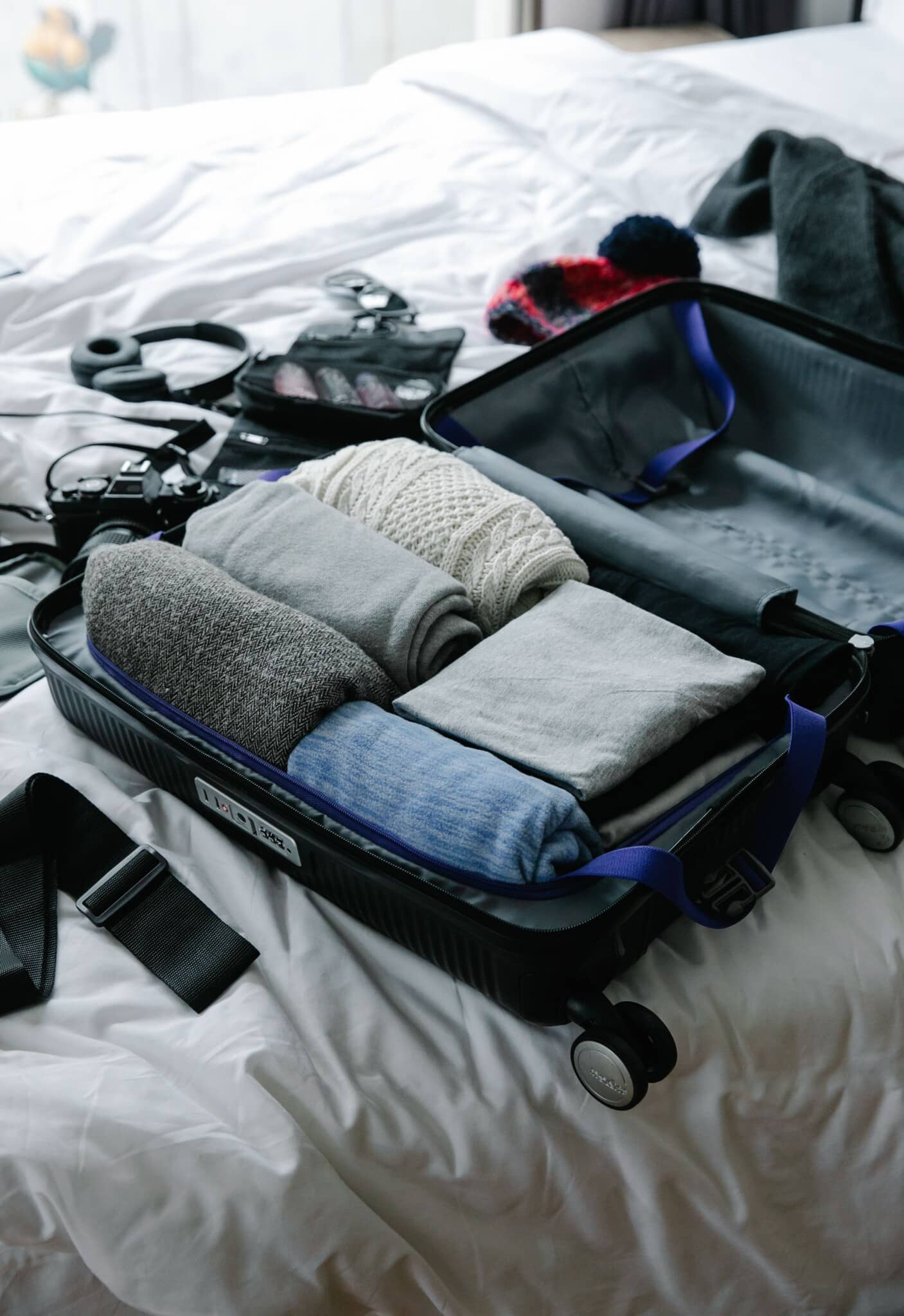 An open suitcase on a bed being packed with neatly folded clothes and travel essentials