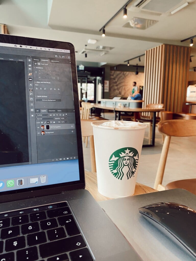 A Starbucks coffee cup next to a laptop on a table in a bright café